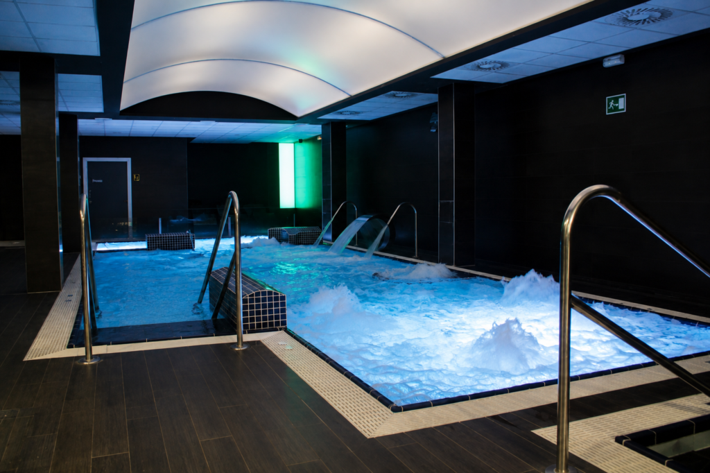 Piscina interior con chorros de agua y luces azules, ideal para spa o centro deportivo.