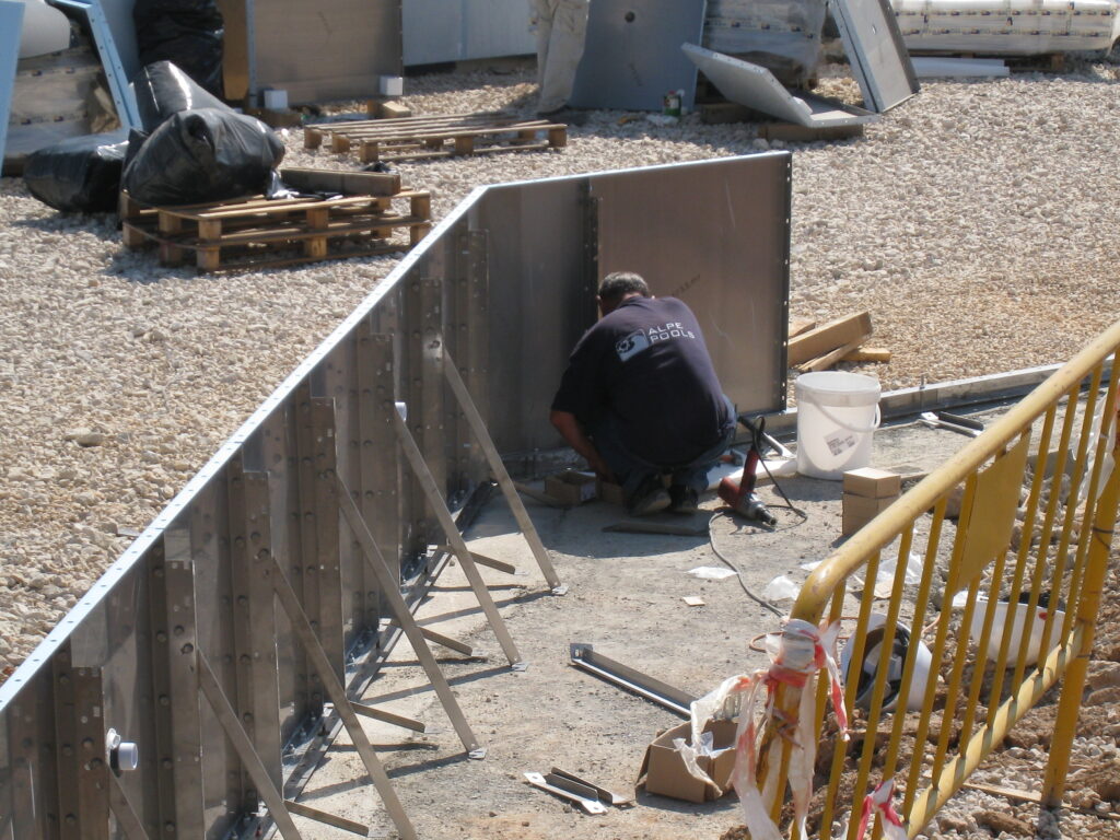 Construcción piscina Myrtha: obrero instala panel en estructura metálica de piscina de verano.