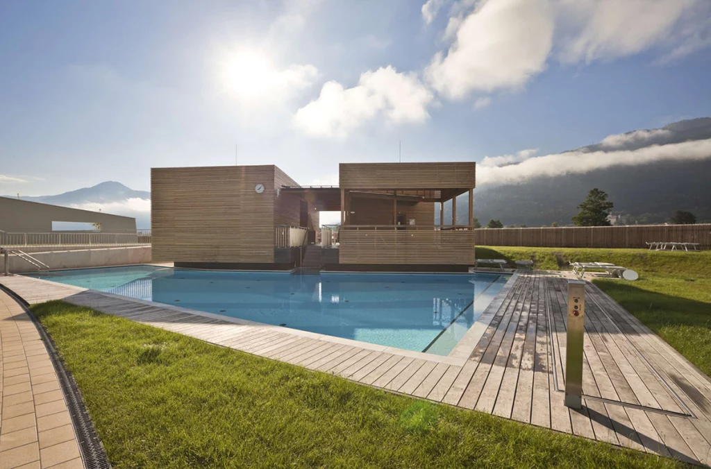 Piscina exterior de diseño Alpe Pools con revestimiento de madera y montañas de fondo.