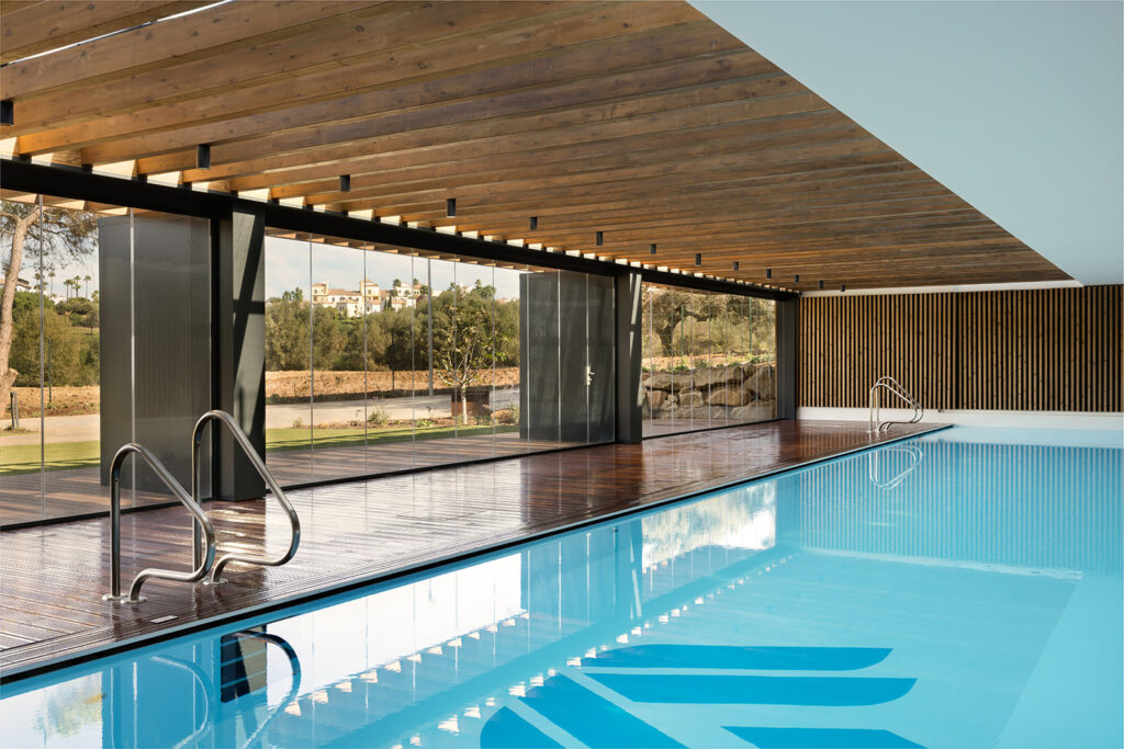 Piscina interior de diseño Village Verde con cubierta de madera y vistas exteriores.