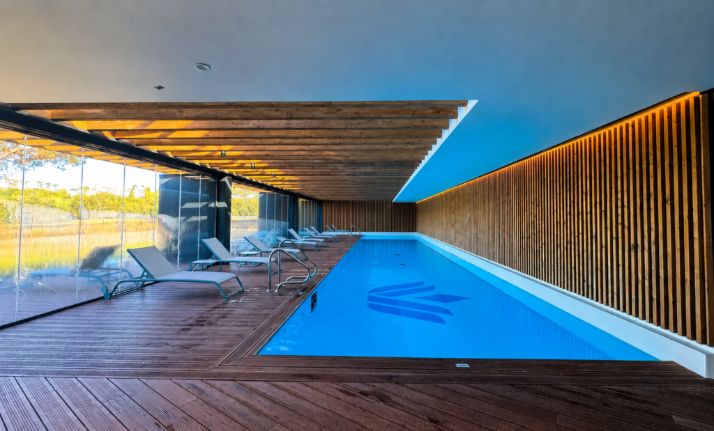 Piscina interior de diseño en Village Verde con tumbonas y acabado de madera.