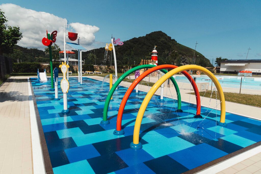 Parque acuático infantil exterior con chorros de agua y toboganes.