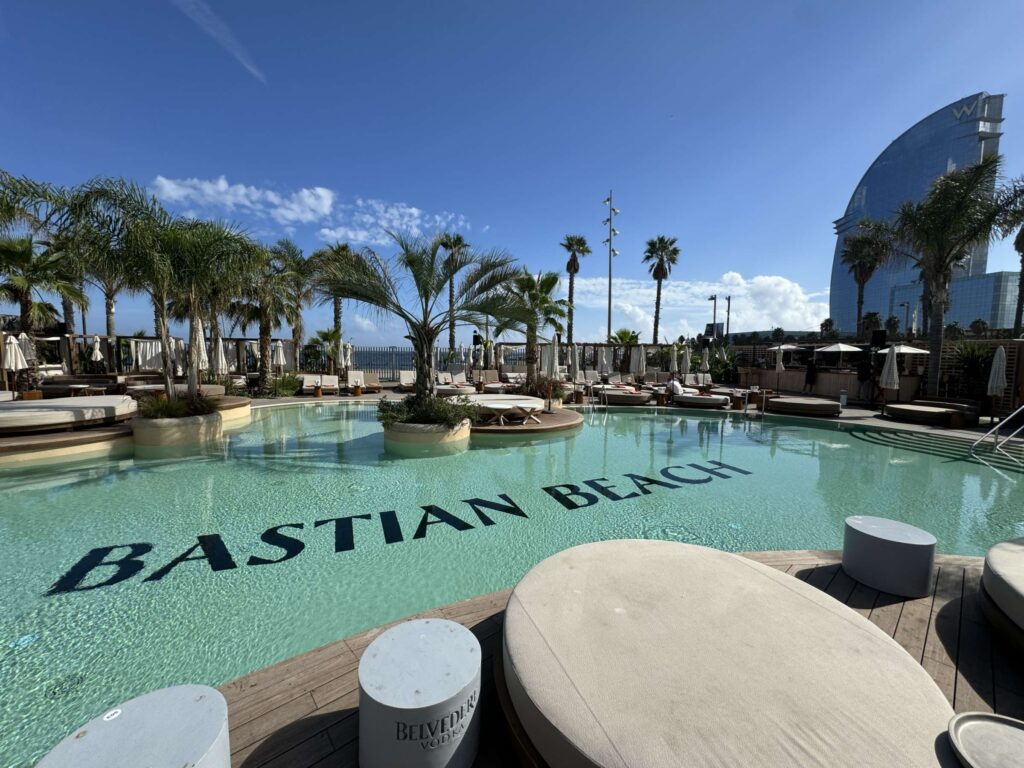 Bastian Beach Club 5 Piscina de diseño en Bastian Beach Club con el nombre del club en el fondo y tumbonas.