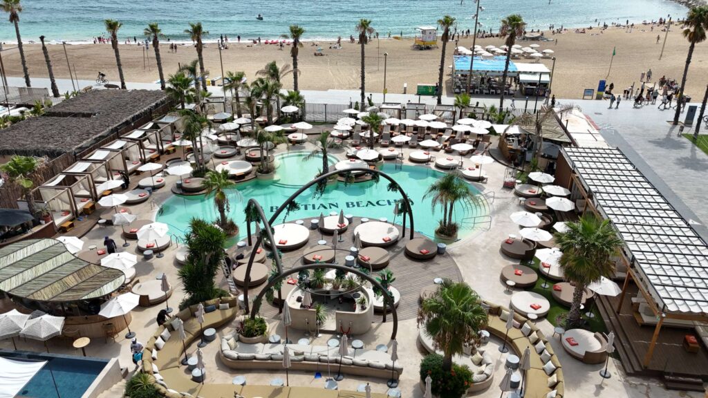 Bastian Beach Club 4 Piscina de diseño en Bastian Beach Club, con tumbonas y palmeras.