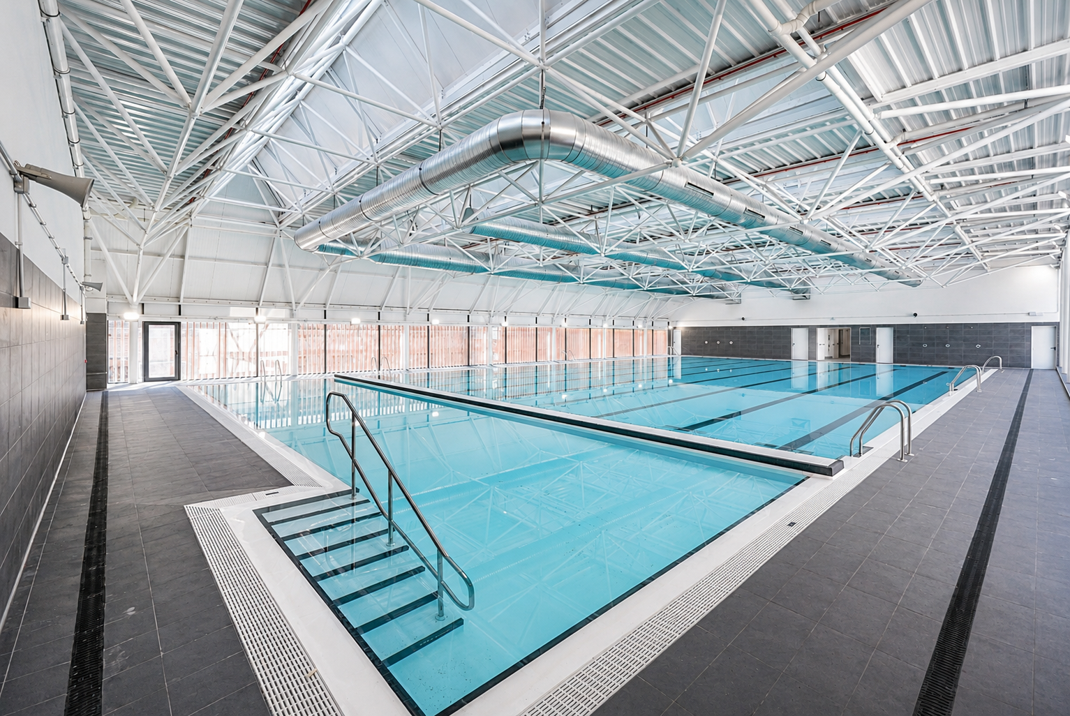 Piscina interior de competición renovada en Madrid, con carriles de natación y estructura metálica.
