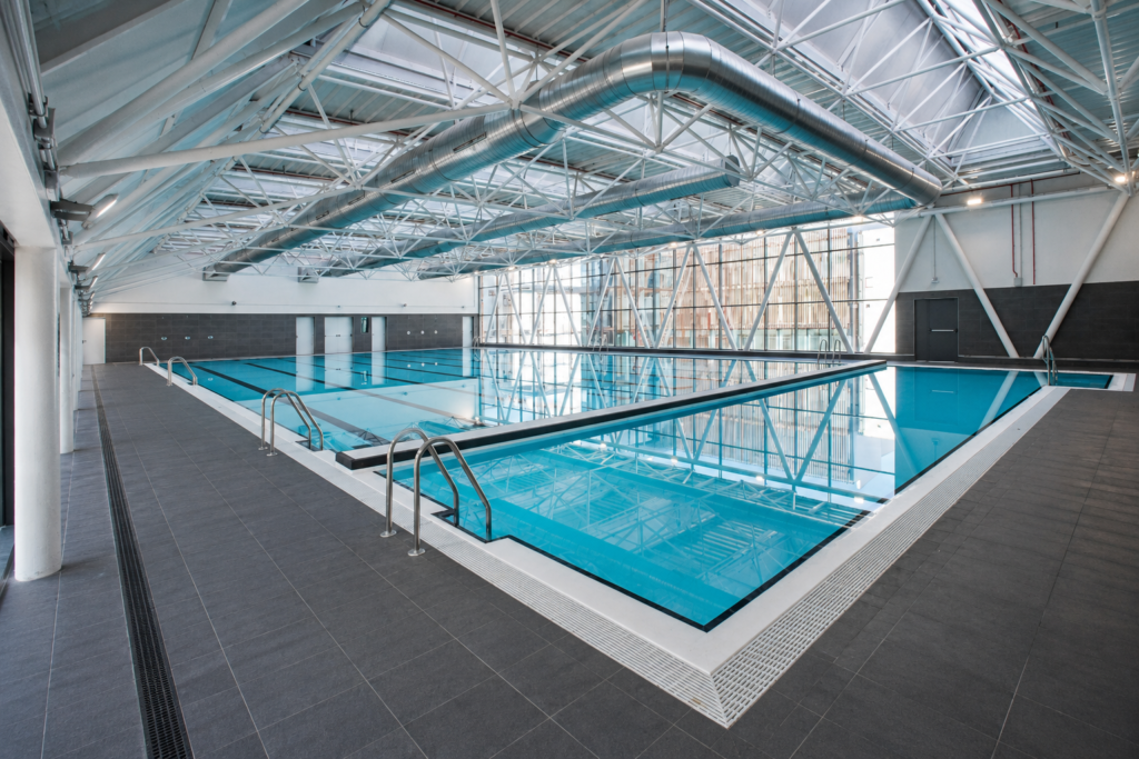 Piscina cubierta de competición renovada, con carriles de natación y estructura metálica.
