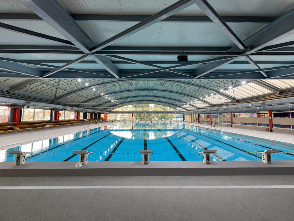 Piscina cubierta de competición en Molins de Rei, con carriles de natación y estructura metálica.