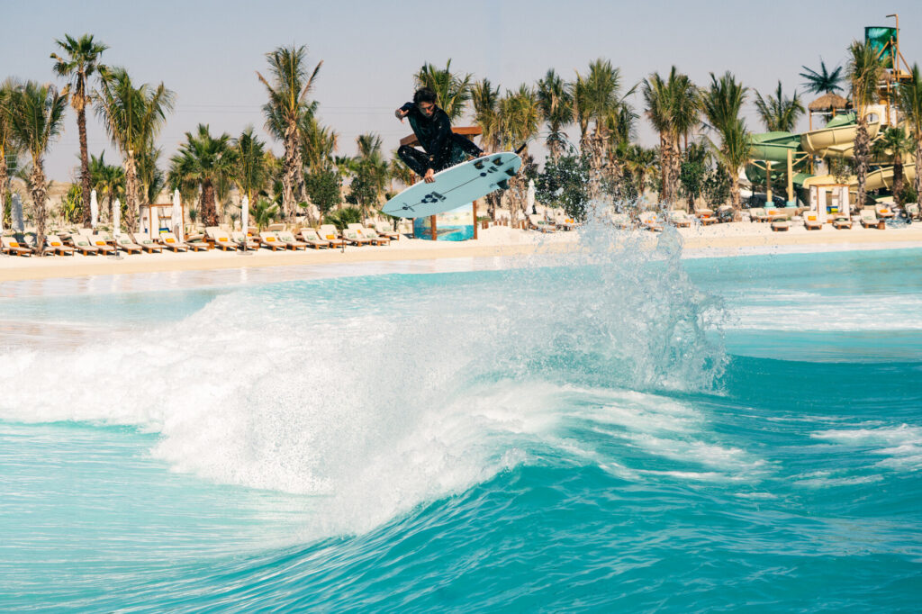 Piscinas de Surf 48 Surfista salta sobre ola en piscina de surf con palmeras y toboganes